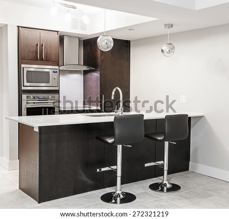 Modern luxury kitchen interior with dark wood cabinets, island counter, bar stools and stainless steel appliances