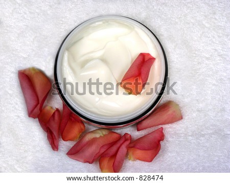 Body cream with rose petals on white towel