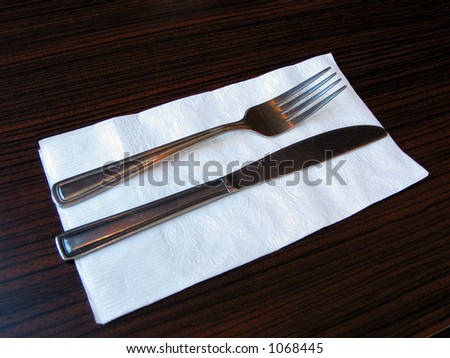 Fork and knife on a white paper napkin, on a table in a restaurant