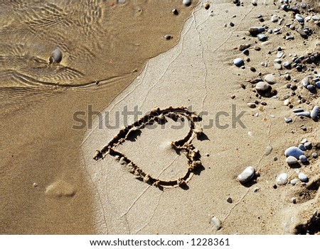 Heart drawn on a sandy beach, about to be washed away by a wave