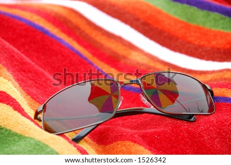 Sunglasses on beach towel reflecting beach umbrella above them
