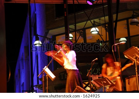 Jazz singer on outdoor stage clapping hands, blurred by long exposure