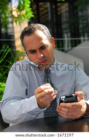 Busy businessman talking on cell phone and working on his palm pilot