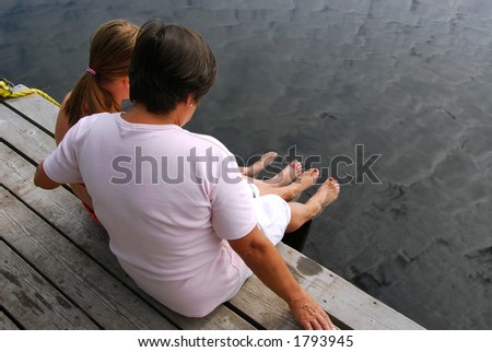 Grandmother and granddaughter sitting on boat dock and dipping feet in water