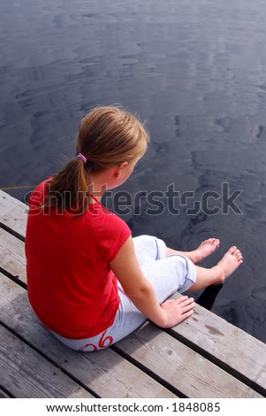 stock photo Young girl sitting on the edge of boat dock dipping her feet 