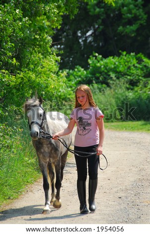 Young girl walking with a pony on a farm road