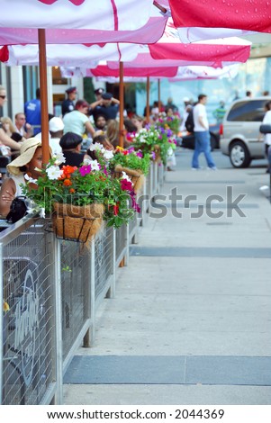 Sidewalk cafe behind a fence decorated with flowers full of people