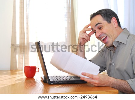 Man sitting at his desk with a laptop and papers looking happy