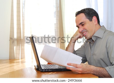 Man sitting at his desk with a laptop and papers looking happy