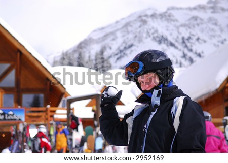 Young girl holding a snowball in front a chalet at downhill ski resort