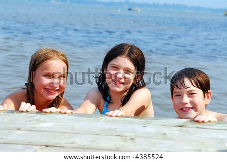 Portrait of three children holding onto wooden dock at the lake