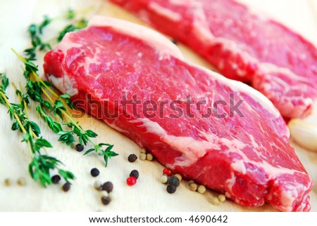Two raw new york steaks on cutting board with thyme and peppercorns