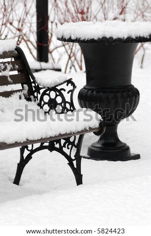Snow covered bench and empty vase in winter park