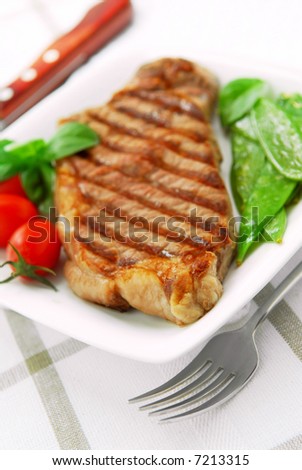 Grilled New York beef steak served on a plate with vegetables