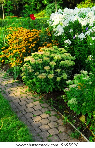 Garden with paved path and blooming flowers in late summer