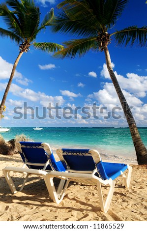 Sandy beach of tropical resort with palm trees and two reclining chairs