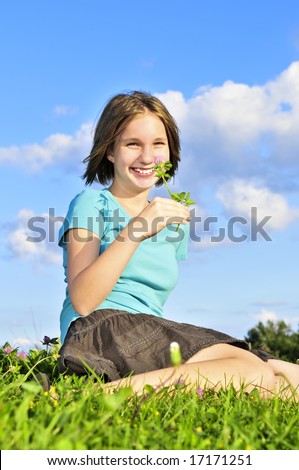 Young teenage girl sitting on grass and smelling a flower