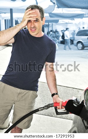 Man filling up a car at a gas station looking horrified