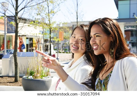 Two young girlfriends at outdoor mall pointing