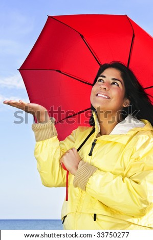 Portrait of beautiful smiling girl wearing yellow raincoat holding red umbrella checking for rain