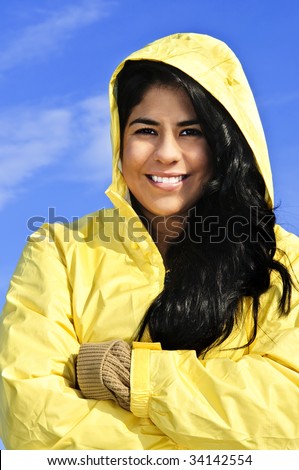 Portrait of beautiful smiling brunette girl wearing yellow raincoat against blue sky