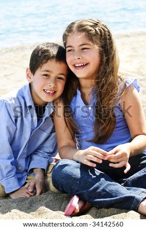 Portrait of brother and sister sitting on sand at the beach