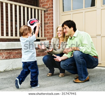 Happy young family playing soccer with toddler on driveway