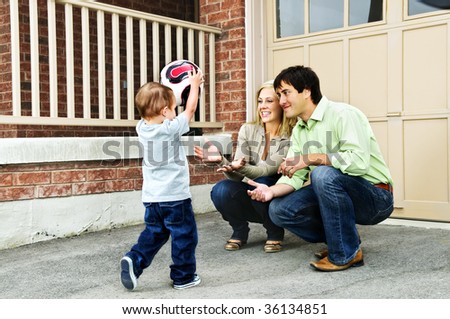 Happy young family playing soccer with toddler on driveway