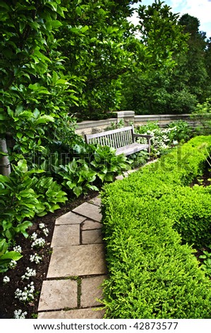 Lush green garden with stone landscaping, hedge, path and bench