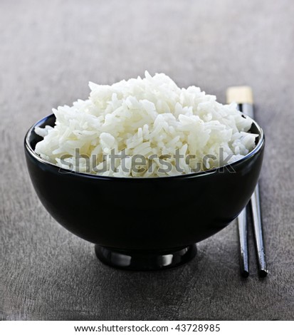 White steamed rice in black round bowl with chopsticks