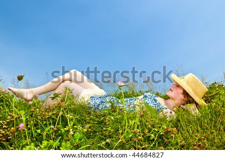 Young teenage girl laying barefoot on summer meadow in straw hat