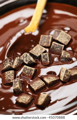 Wooden spoon stirring melting rich chocolate chunks