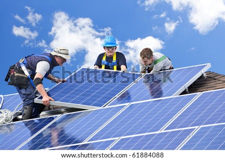 Workers installing alternative energy photovoltaic solar panels on roof