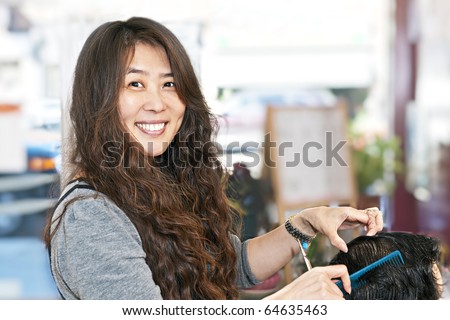 Happy hairdresser cutting hair in her salon