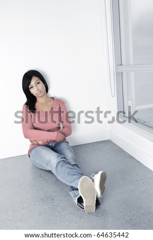 Depressed young black woman sitting against wall on floor