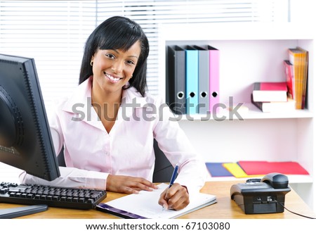 Smiling young black business woman writing at desk in office