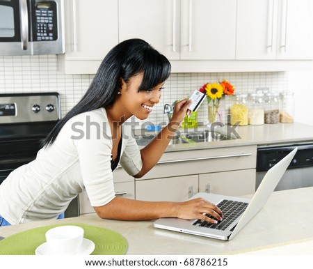 Smiling black woman online shopping using computer and credit card in kitchen