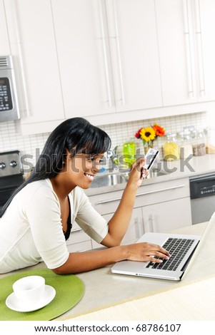 Smiling black woman online shopping using computer and credit card in kitchen