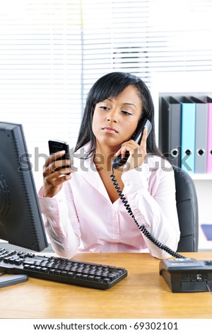 Young black business woman multitasking using two phones in office