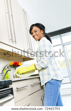 Happy smiling young black woman enjoying washing dishes in kitchen
