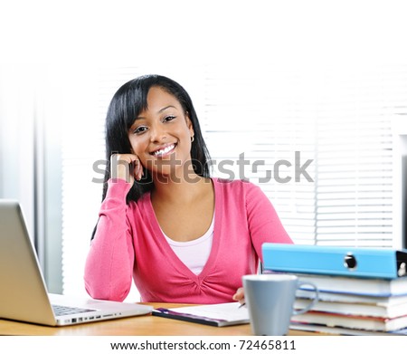 Smiling young black female student with computer and textbooks at desk