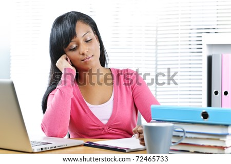 Young black female student studying at desk with books and laptop