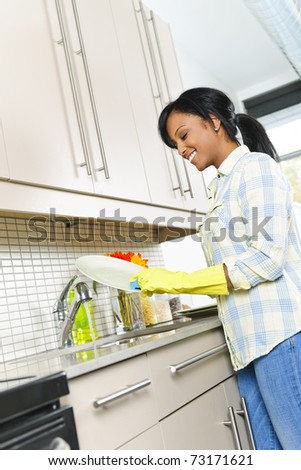 Smiling young black woman washing dishes in kitchen