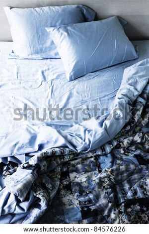 Unmade messy bed with wrinkled sheets from above