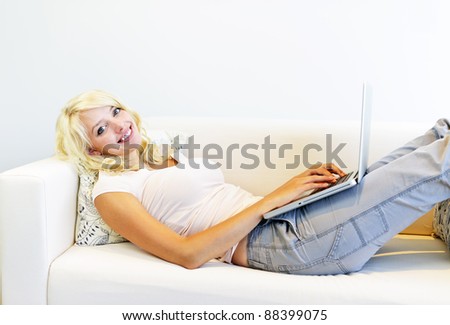 Smiling young blonde woman using laptop computer laying on couch