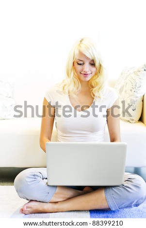 Happy blonde woman sitting on floor with computer near couch