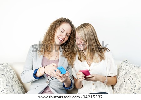 Two smiling women using mobile devices with colorful cases