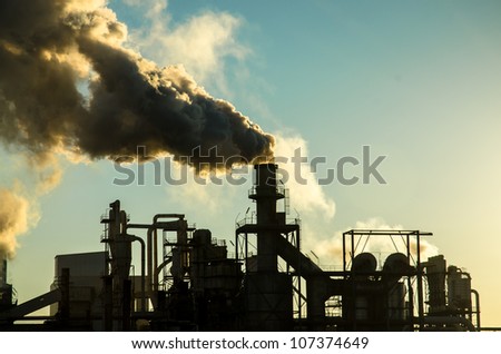 Smoking chimney  at sunset on industrial buildings complex.