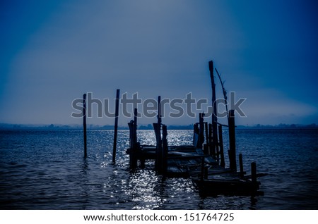 Old fishing dock with moon light reflection on calm water.