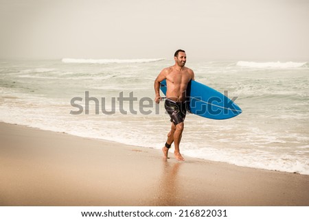 Surfer running on the beach with his surfboard.
